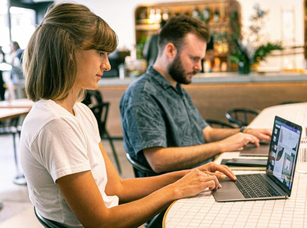 Two young professionals working on laptops in a modern cafe setting.